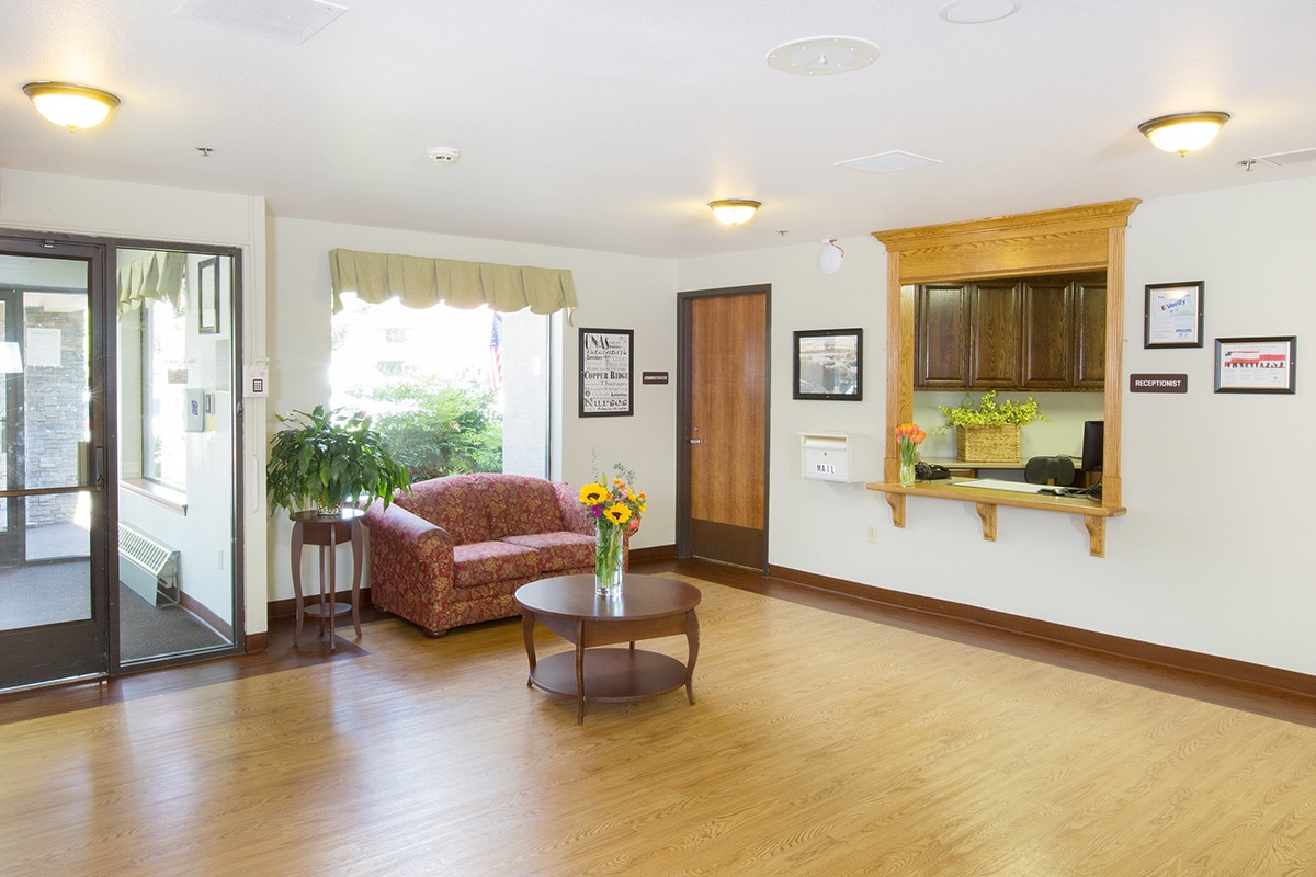 Spacious lobby with a red sofa, a vase of sunflowers, and a receptionist window
