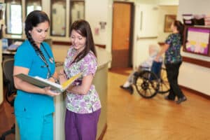 Two female nurses standing at lobby desk, looking through files