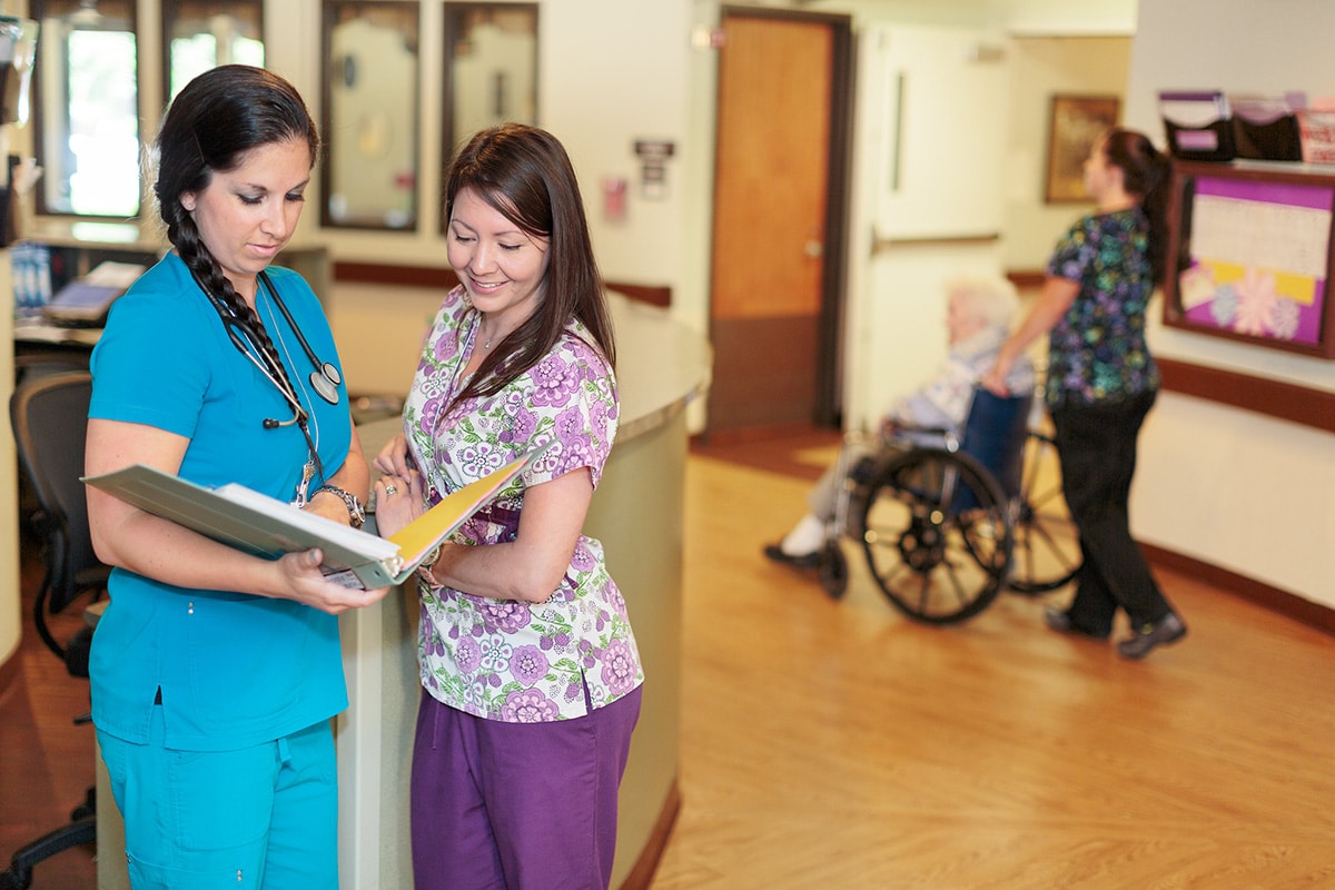 Two female nurses standing at lobby desk, looking through files
