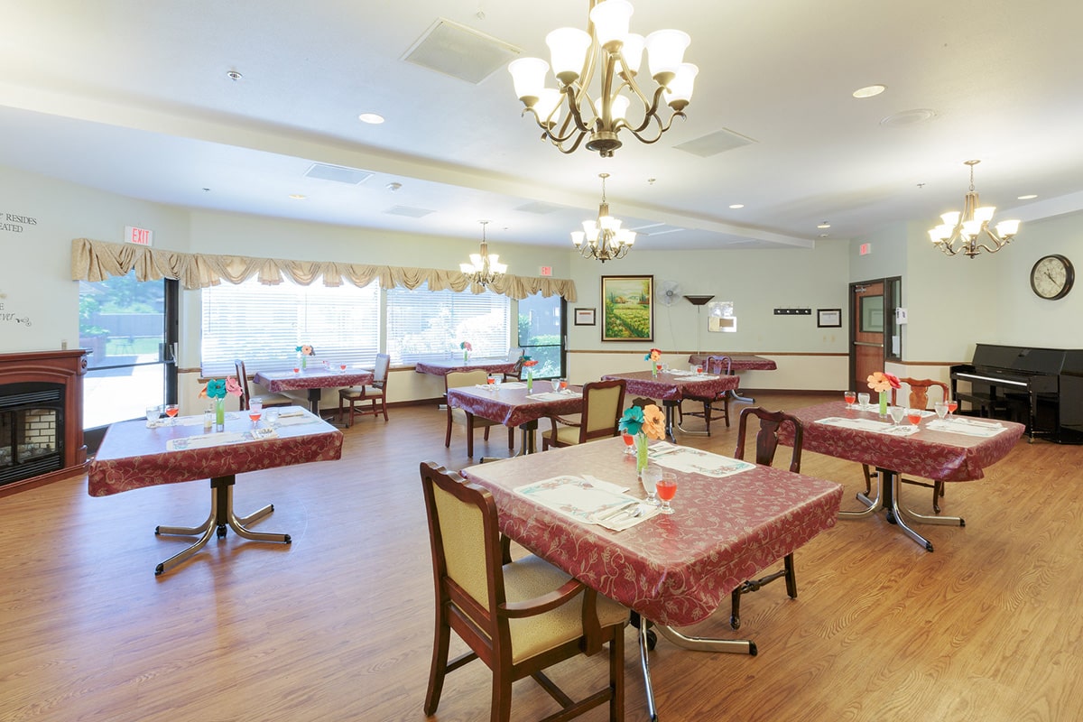 Dining room with tables with red tablecloths, colorful paper flowers on top, and a piano